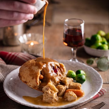 A plate of Christmas pie and veg with pouring gravy over the meal